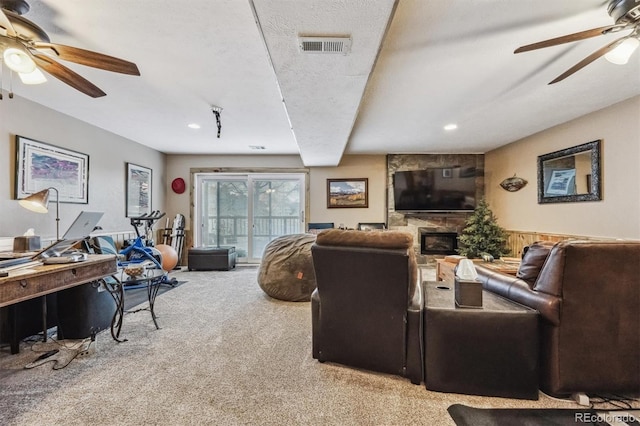 living room featuring ceiling fan, a textured ceiling, a stone fireplace, carpet flooring, and visible vents