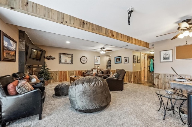 living area with wooden walls, a ceiling fan, carpet flooring, and wainscoting