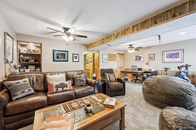 living room featuring built in shelves, ceiling fan, a textured ceiling, and carpet flooring