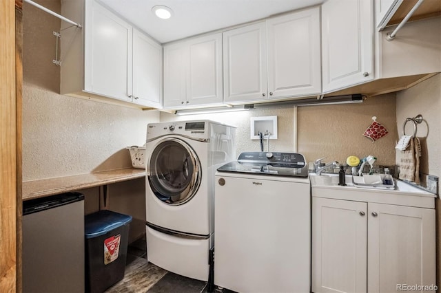 washroom featuring a textured wall, washer and clothes dryer, a sink, and cabinet space