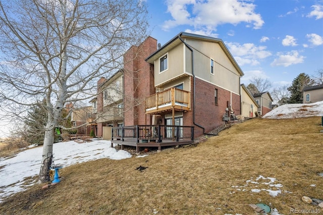 snow covered back of property with a chimney, a deck, a lawn, and brick siding