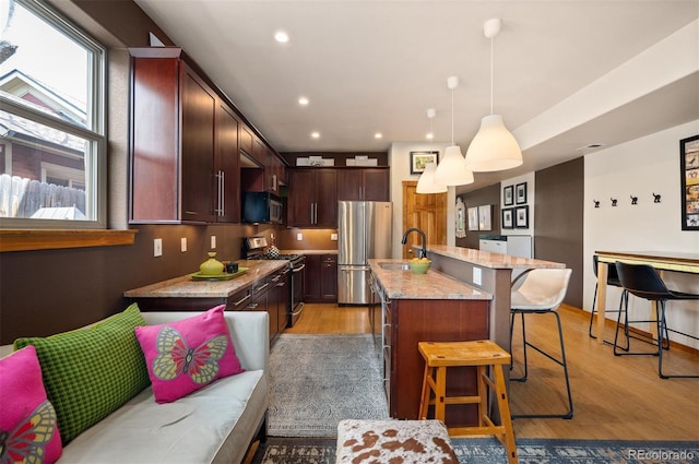 469 Elati St, Denver, CO 80204 - kitchen with a kitchen island with sink, appliances with stainless steel finishes, a sink, a breakfast bar, and light wood-style flooring