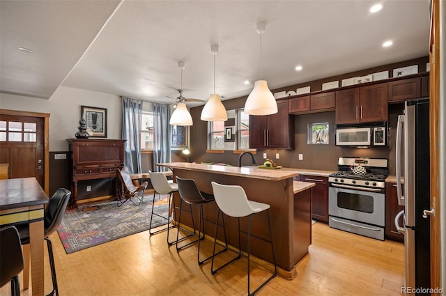 469 Elati St, Denver, CO 80204 - kitchen featuring a kitchen breakfast bar, pendant lighting, appliances with stainless steel finishes, a center island with sink, and light wood finished floors