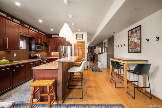 469 Elati St, Denver, CO 80204 - kitchen with a kitchen island with sink, a breakfast bar, light stone countertops, light wood-style flooring, and appliances with stainless steel finishes