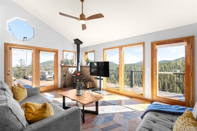 living room with ceiling fan, high vaulted ceiling, light hardwood / wood-style flooring, and a wood stove