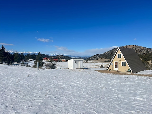 yard layered in snow featuring a mountain view and a storage unit