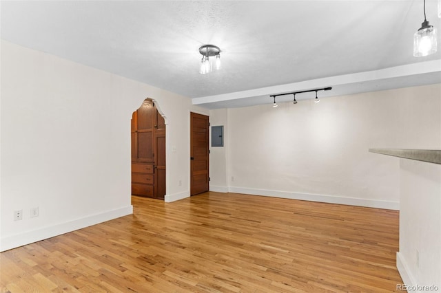 spare room featuring light hardwood / wood-style floors, rail lighting, a textured ceiling, and electric panel