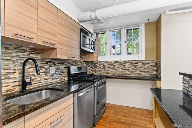 kitchen featuring sink, decorative backsplash, dark stone counters, and appliances with stainless steel finishes