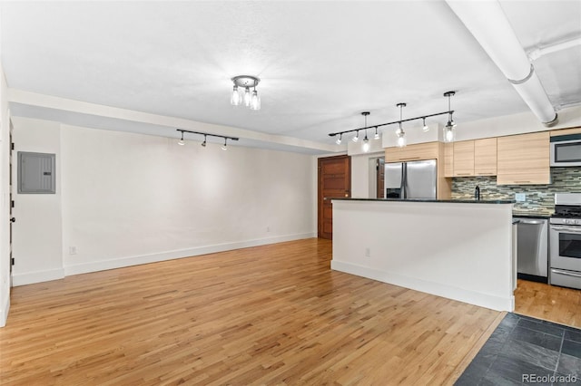 kitchen featuring dark countertops, backsplash, electric panel, light wood-style floors, and stainless steel appliances