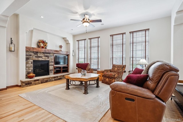 living room featuring hardwood / wood-style floors, a stone fireplace, a wealth of natural light, and ceiling fan