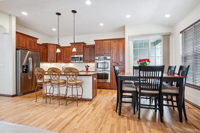 kitchen with decorative light fixtures, light hardwood / wood-style flooring, a kitchen breakfast bar, a kitchen island, and stainless steel appliances