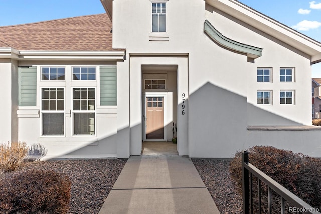 property entrance with roof with shingles and stucco siding