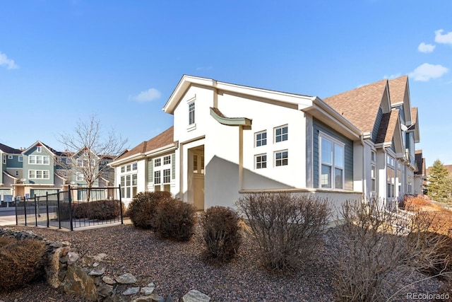 view of side of home with stucco siding, a residential view, a shingled roof, and fence