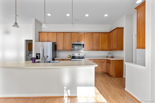 kitchen featuring light wood finished floors, light countertops, appliances with stainless steel finishes, brown cabinetry, and a sink