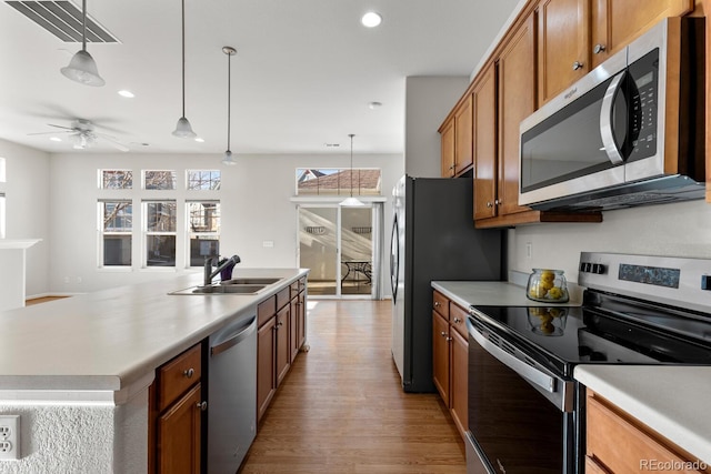 kitchen with pendant lighting, light countertops, appliances with stainless steel finishes, brown cabinetry, and a sink