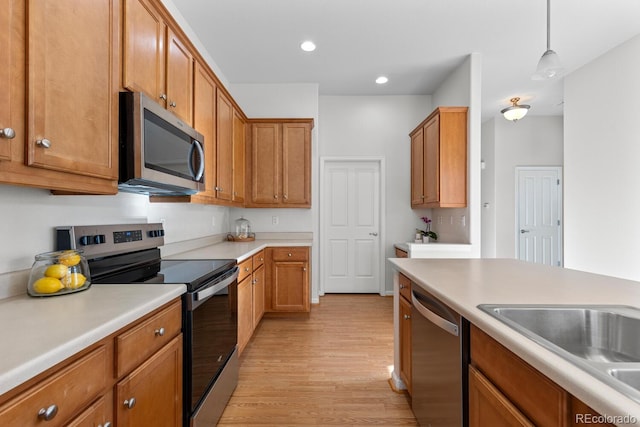 kitchen with light wood-type flooring, light countertops, hanging light fixtures, stainless steel appliances, and a sink