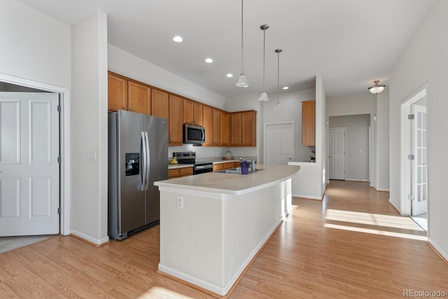 kitchen with light wood finished floors, appliances with stainless steel finishes, light countertops, and a kitchen island with sink