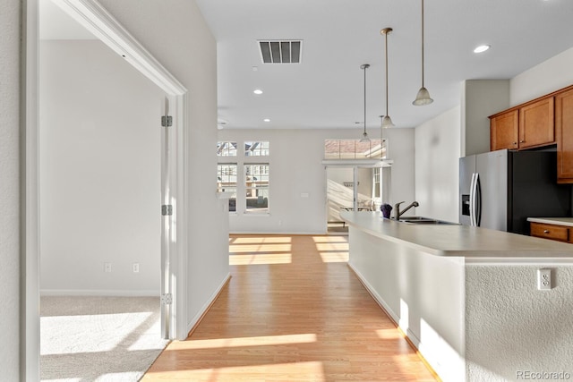 kitchen featuring visible vents, stainless steel fridge with ice dispenser, a sink, hanging light fixtures, and brown cabinets