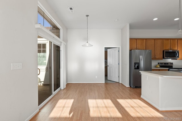 kitchen featuring light wood finished floors, baseboards, hanging light fixtures, brown cabinetry, and stainless steel appliances