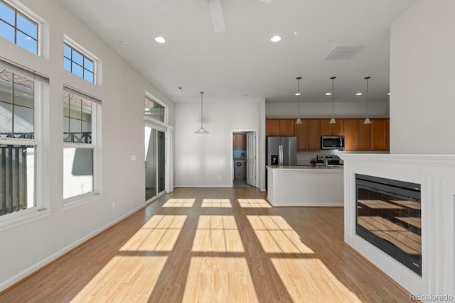 kitchen with visible vents, pendant lighting, appliances with stainless steel finishes, brown cabinetry, and light wood finished floors