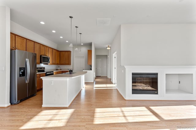 kitchen with visible vents, a glass covered fireplace, appliances with stainless steel finishes, brown cabinetry, and light wood finished floors