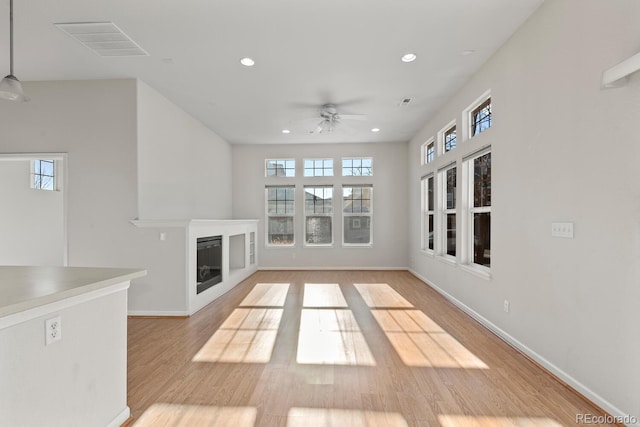 unfurnished living room with recessed lighting, light wood-style flooring, plenty of natural light, and a glass covered fireplace