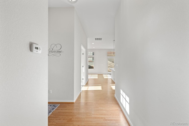 hallway featuring visible vents, baseboards, and light wood finished floors