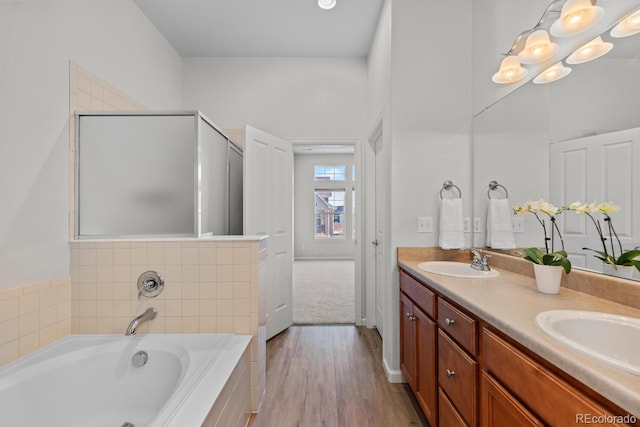 bathroom with double vanity, wood finished floors, a bath, an enclosed shower, and a sink