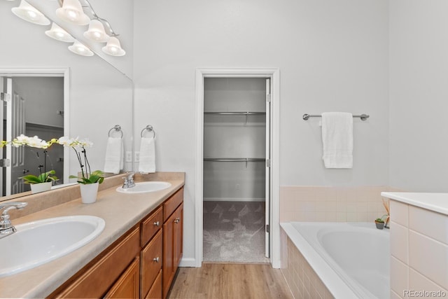 bathroom with double vanity, wood finished floors, a bath, and a sink