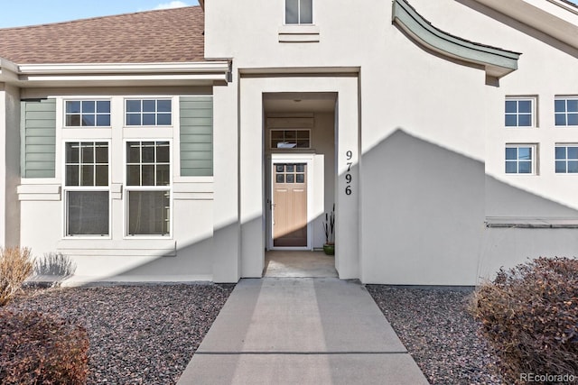 property entrance featuring stucco siding and a shingled roof