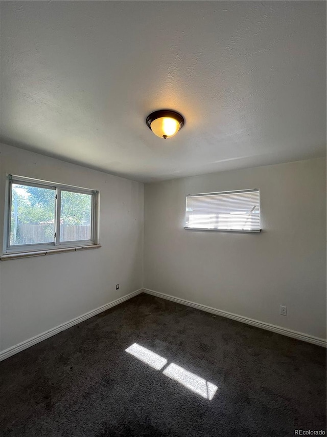 unfurnished room featuring a textured ceiling and dark carpet