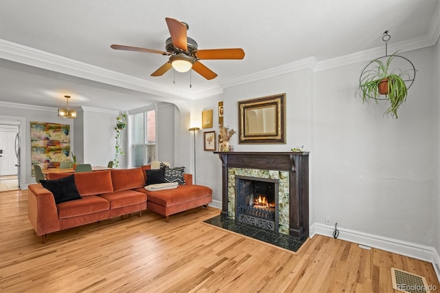 living room with a high end fireplace, ornamental molding, ceiling fan, and light wood-type flooring