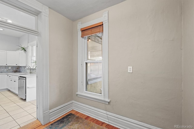 interior space with white cabinetry, decorative backsplash, stainless steel dishwasher, and a healthy amount of sunlight