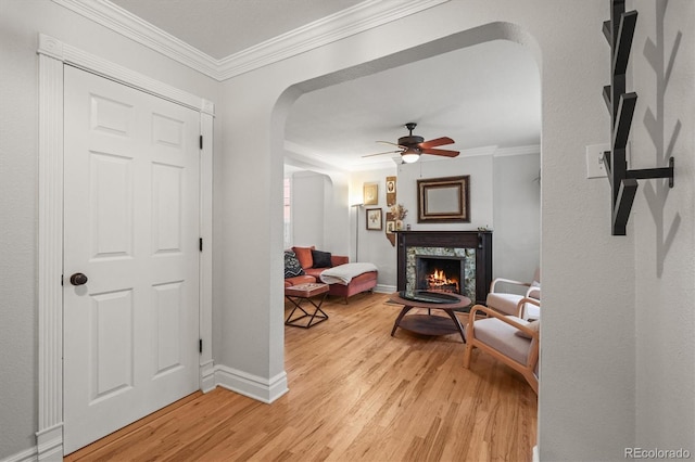2336 N High St, Denver, CO 80205 - living room featuring arched walkways, light wood-type flooring, ceiling fan, crown molding, and a warm lit fireplace
