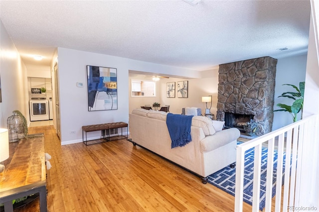 living room featuring a textured ceiling, a fireplace, washer / clothes dryer, and light wood-style floors