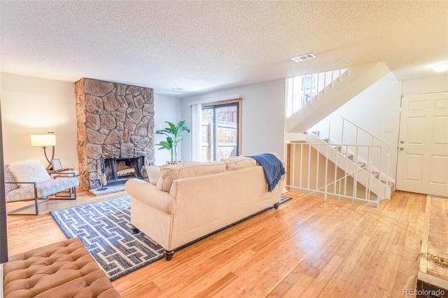 living room featuring wood finished floors, visible vents, a fireplace, stairs, and a textured ceiling