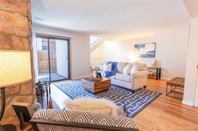 living area featuring light wood-type flooring, visible vents, baseboards, and a textured ceiling