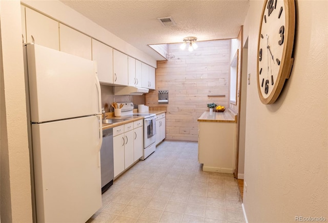 kitchen with visible vents, wooden walls, under cabinet range hood, light countertops, and white appliances