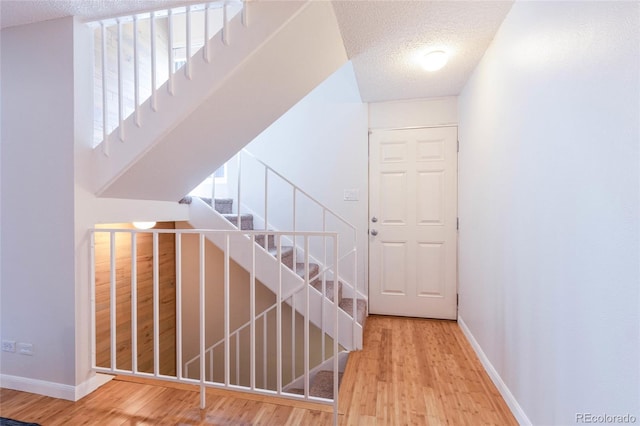 stairs featuring a textured ceiling, baseboards, and wood finished floors