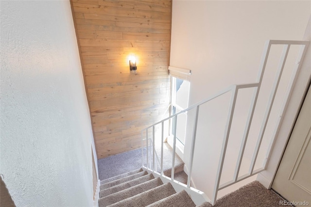 stairs with wooden walls, carpet flooring, and a textured wall