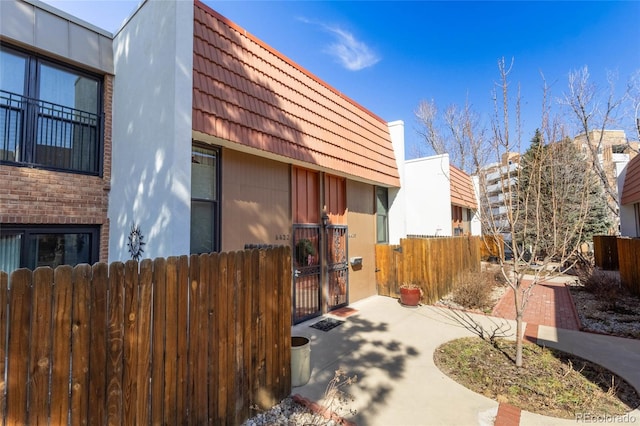 view of home's exterior featuring a gate, a tiled roof, mansard roof, and fence