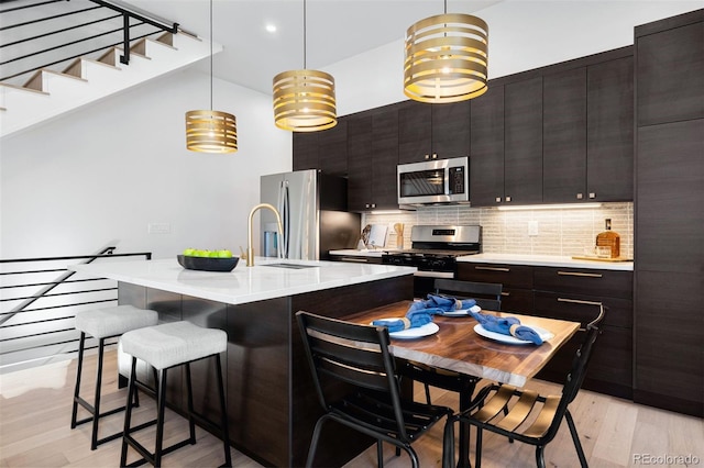 kitchen featuring hanging light fixtures, a center island with sink, stainless steel appliances, and light countertops