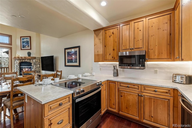 kitchen with tasteful backsplash, dark hardwood / wood-style flooring, kitchen peninsula, a fireplace, and appliances with stainless steel finishes