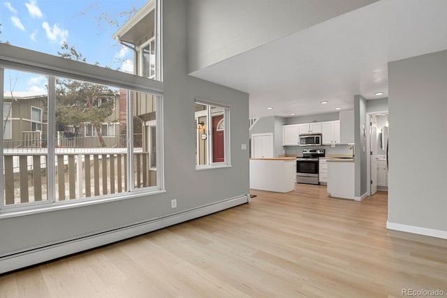 unfurnished living room with light wood finished floors, baseboards, a baseboard radiator, recessed lighting, and a sink