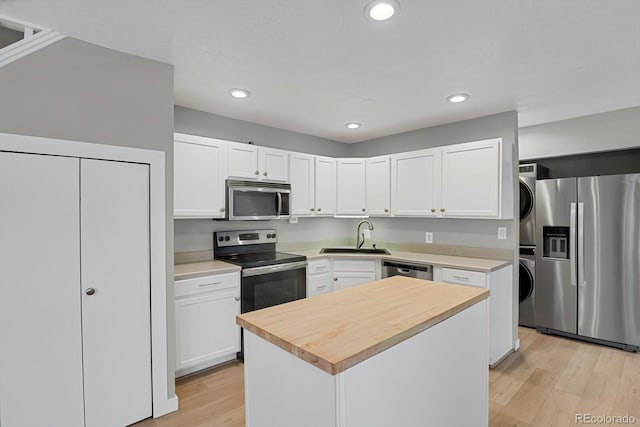 kitchen featuring stacked washing maching and dryer, a sink, white cabinets, appliances with stainless steel finishes, and light wood-type flooring