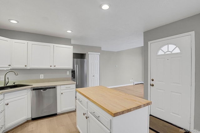 kitchen with a sink, appliances with stainless steel finishes, wood counters, white cabinetry, and a baseboard heating unit