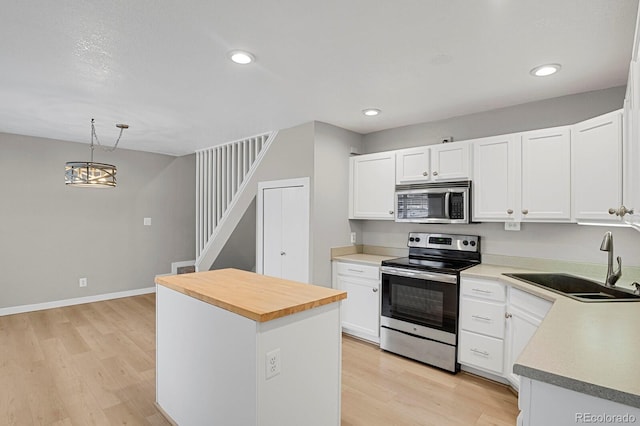 kitchen featuring light wood finished floors, a kitchen island, butcher block countertops, appliances with stainless steel finishes, and a sink