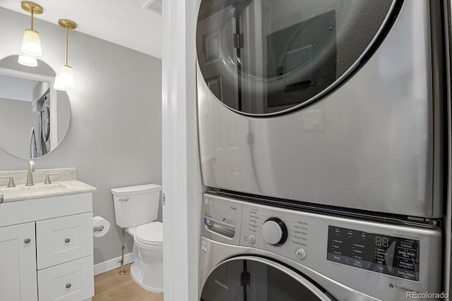 bathroom with visible vents, toilet, stacked washing maching and dryer, wood finished floors, and vanity