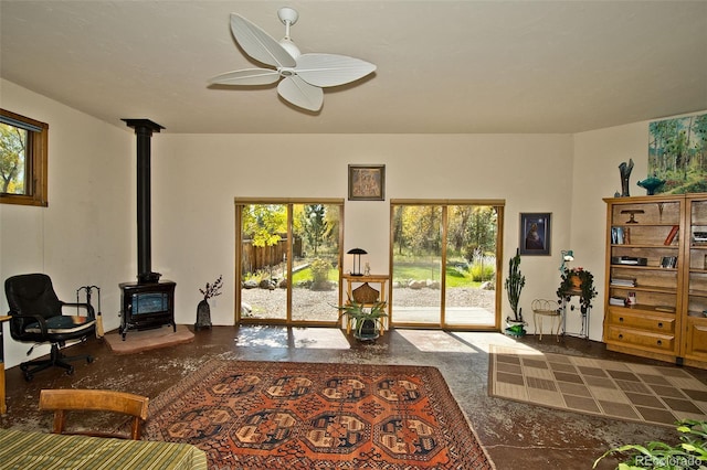 living room featuring ceiling fan, plenty of natural light, and a wood stove