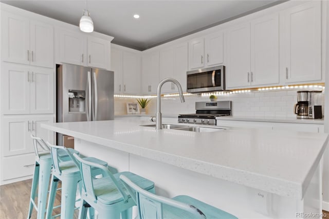 kitchen with appliances with stainless steel finishes, hanging light fixtures, light countertops, a kitchen bar, and a sink